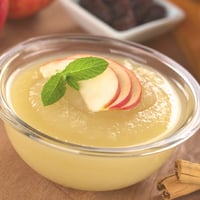 Homemade applesauce in a jar garnished with sliced red apples.