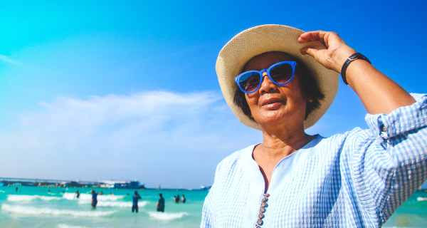 Senior woman protecting herself from the sun by wearing a sun hat, sun glasses, and long sleeves.