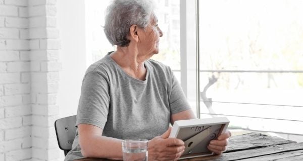 Senior holding a framed image and looking out the window.