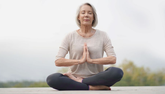 Senior woman seated on the ground in yoga pose.