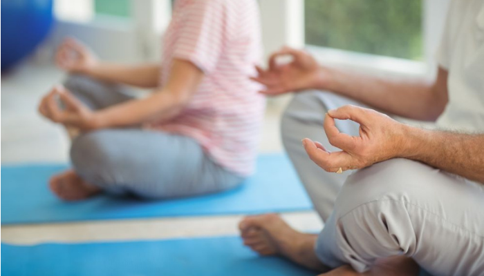 Senior man and woman seated on exercise mats in yoga poses.