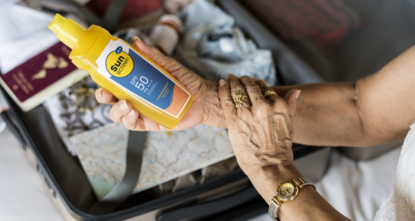 Woman holding a bottle of sunscreen and applying to her skin to protect it from the sun.