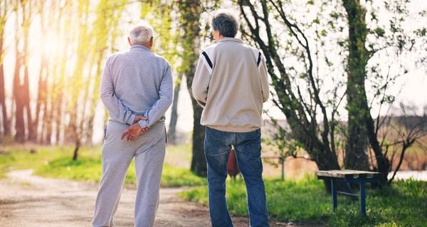 A man with dementia walking outdoors with a friend.