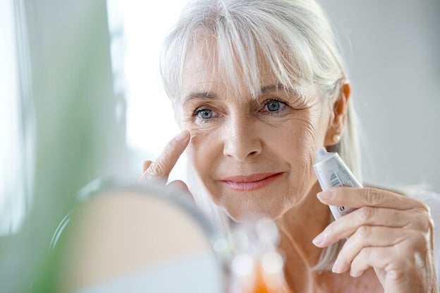 Senior woman applies moisturizer as part of skin care routine