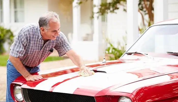 Smiling older man polishing a vintage red car in a driveway