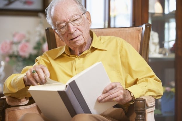 Senior man in yellow shirt studies from book