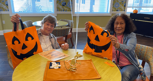 Two senior women sitting at a table and holding up Halloween bags