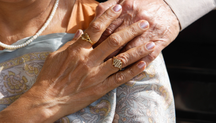 Woman holding a man’s hand that was placed on her shoulder. 