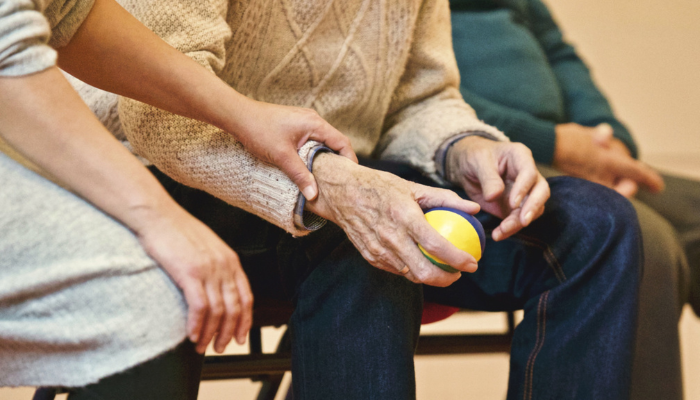 Mature adult playing with a ball under the guidance of another adult. 