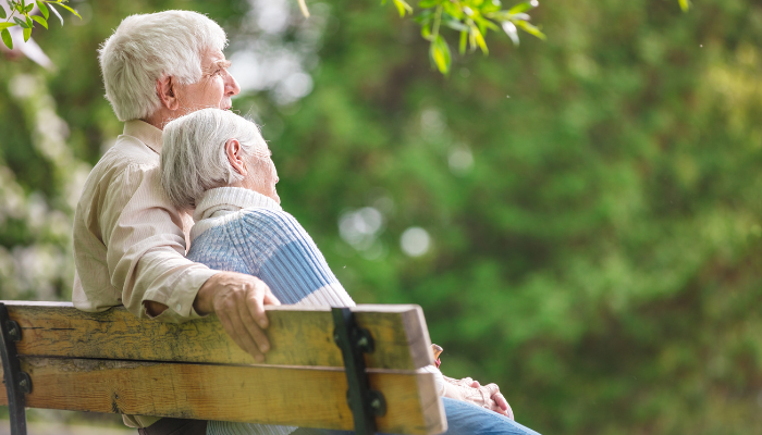 Mature couple sitting on a park bench with the woman’s head on the man’s shoulder. 