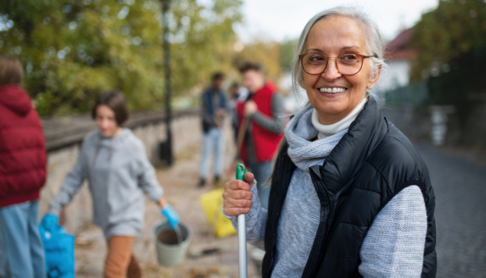 Mature woman holding a broom as she cleans up her community.