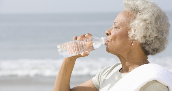 Senior woman on the beach drinking a bottle of water to keep hydrated.