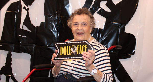 senior woman posing with doll face sign 