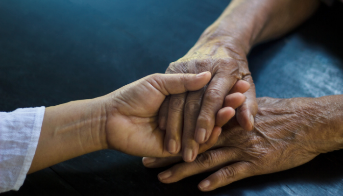 adult child holding the hand of her elderly parent with Alzheimer's