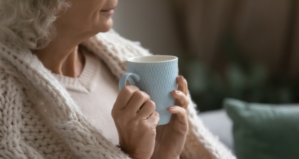 Senior woman keeping warm wrapped in a blanket while enjoying a hot drink.