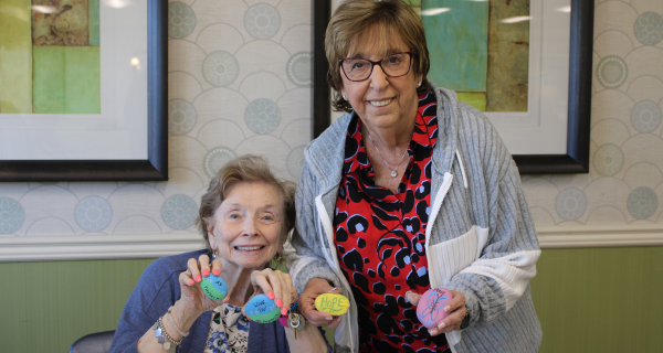 Two smiling senior residents display the brightly colored rocks that they created in honor of World Kindness Day