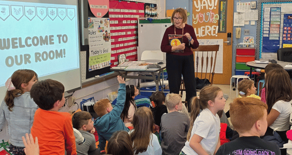 Massapequa resident stands in front of a group of elementary students, reading a story and answering questions.