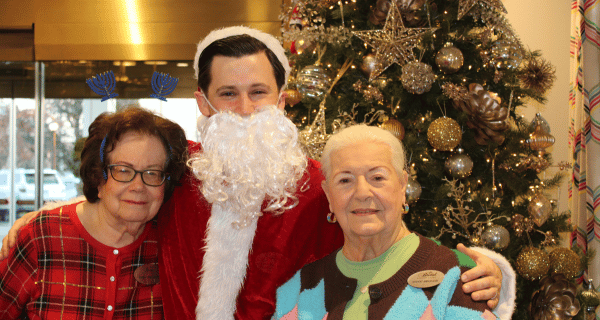 Two residents stand on either side of a team member dressed as Santa in front of the beautifully decorated tree