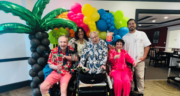 Residents at The Bristal at Garden City pose for pictures in front of a colorful, luau-inspired balloon arch.