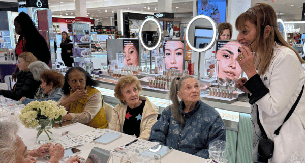 Seniors seated at a table at the Clinique counter while a professional demonstrates various products and their uses.