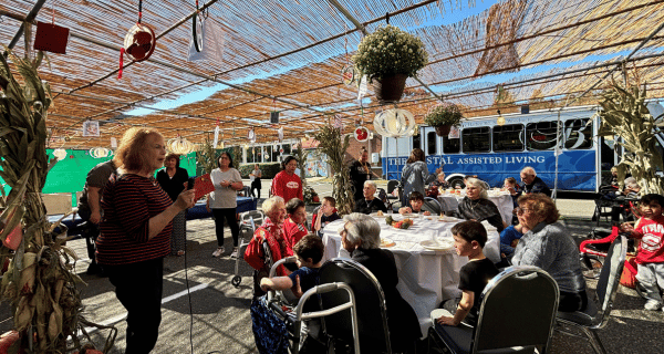 Residents and children who attend preschool at the HERJC sit together under the sukkah and listen to a story being read.