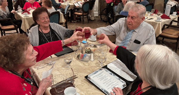 4 senior residents seated around a dining table raise wine glasses for a toast to the holiday season