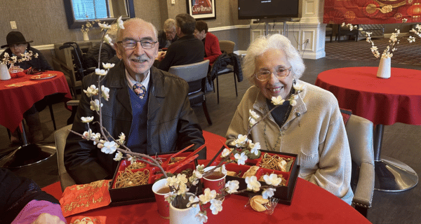 Two residents sit together at a table adorned with red decorations, cherry blossoms, and a bento box lunch.