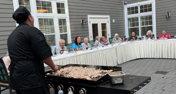 Chef John stands at the flat-top grill, cooking chicken, while entertaining residents of The Bristal at Wayne.