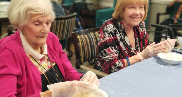 senior women seated at table making cookies together