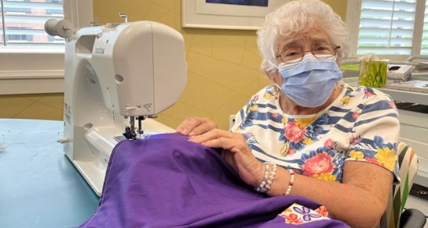 senior woman using sewing machine to sew purple cape