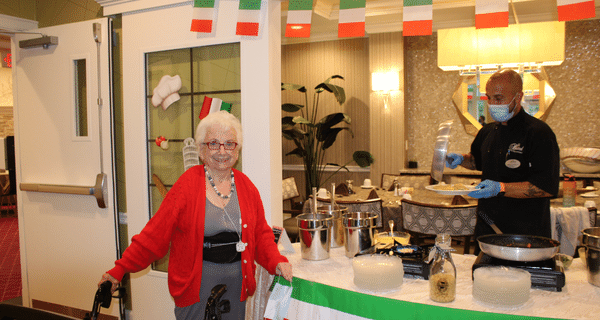 senior woman standing next to chef preparing pasta