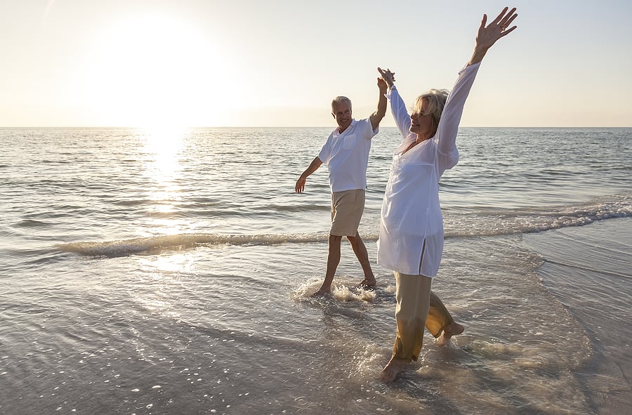 Healthy seniors walking along the beach holding hands and celebrating