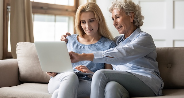 An older mother and daughter sit on couch at home with a laptop