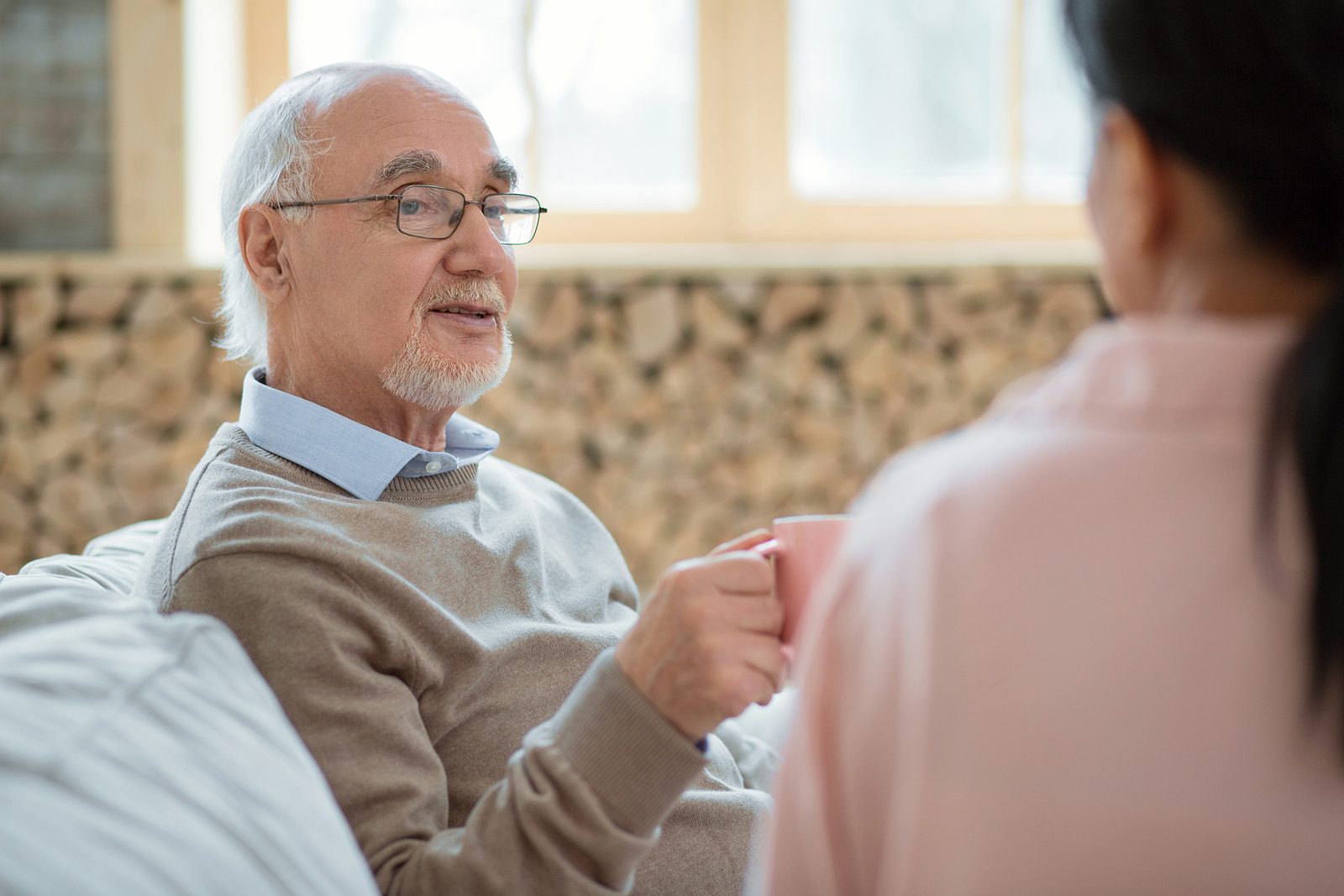 Older man sitting on couch with tea talking to younger woman