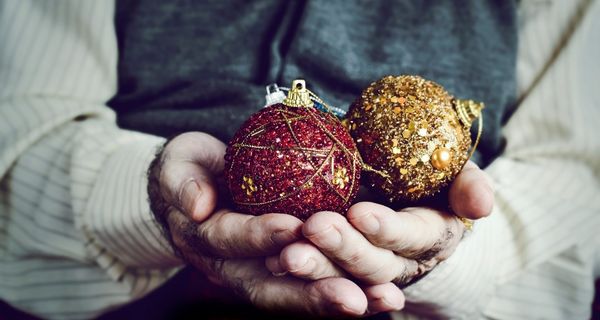 Mature person holding two glittery beaded red and gold holiday ornaments.