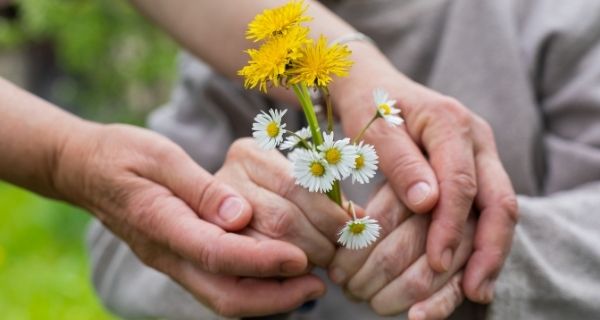 A caregiver’s hands holding a senior’s hands that are holding flowers. 