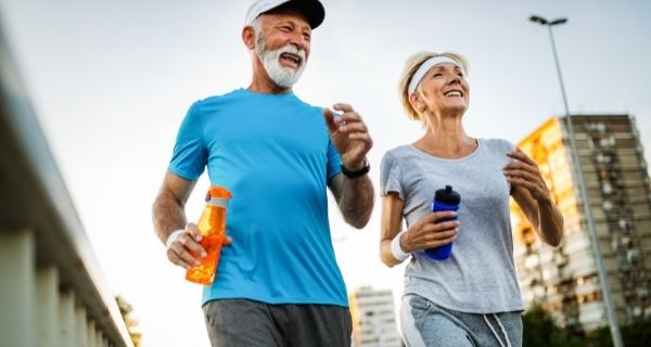 Senior man and woman practicing lifestyle medicine my taking a brisk walk and staying hydrated.