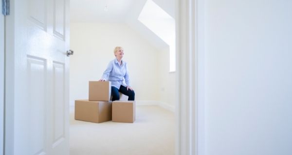 Older woman sitting on packed boxes in the home she is selling.