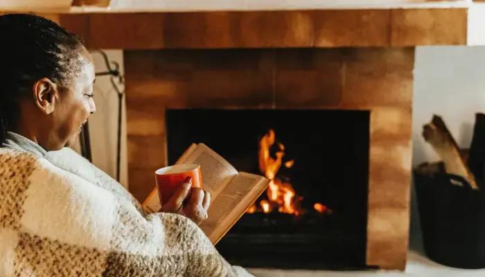 Senior woman cozied up by the fire with a book and coffee.