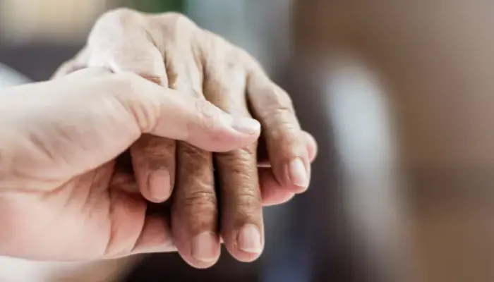 Caregiver holding a senior’s hand that’s living with Alzheimer’s.