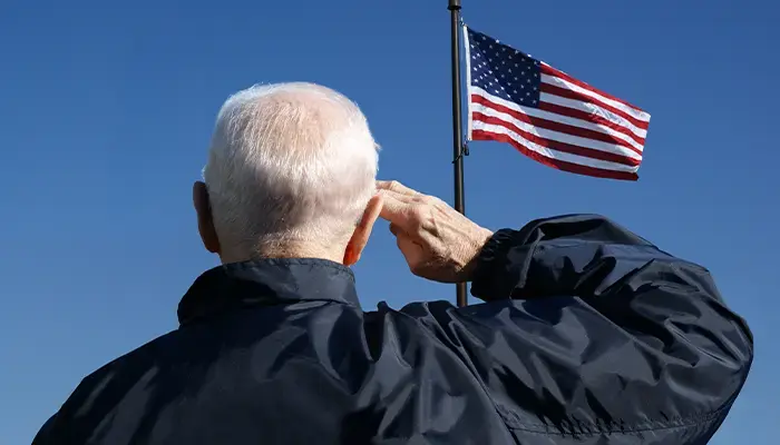 Elderly veteran saluting the American flag against a clear blue sky