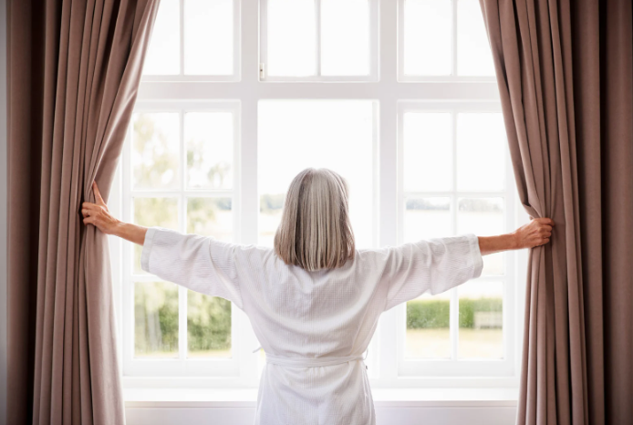 Older woman opening window curtains in her luxury senior living apartment