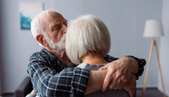 Mature adult man hugging and kissing his wife who is suffering from Alzheimer’s Disease. 