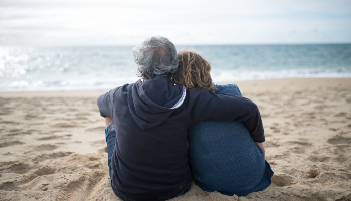 An elderly couple sitting on the beach looking at the water contemplating a big decision. 