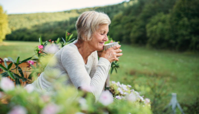 A mature adult woman sipping her coffee outdoors in nature on a beautiful summer day. 