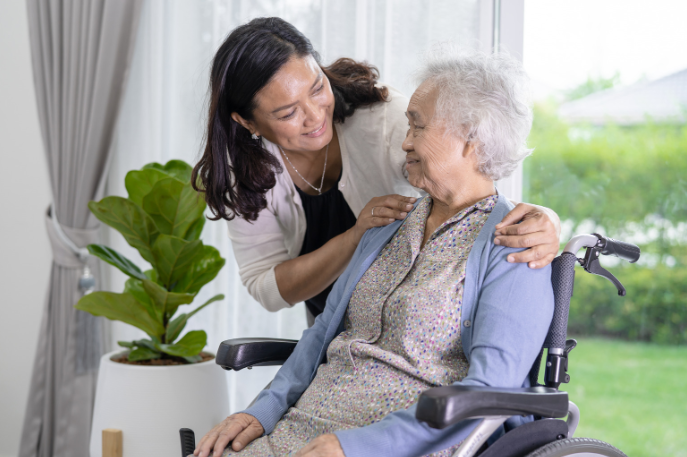 Younger woman caregiver holding hand of older woman in wheelchair in an upscale home.