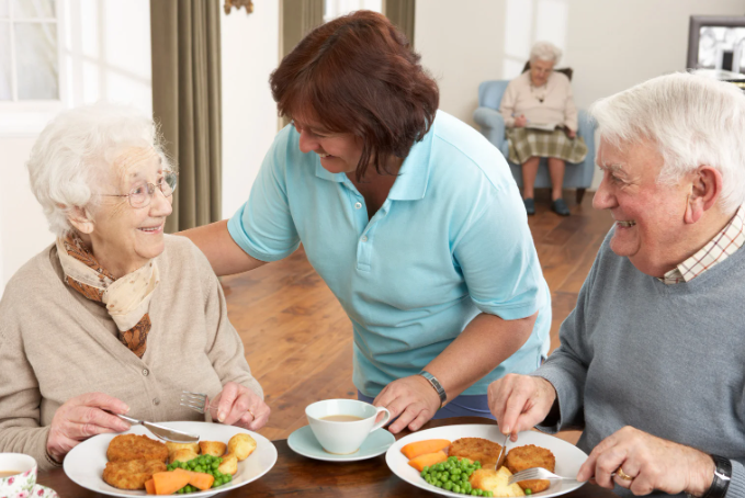 Senior couple eating dinner with aid serving them